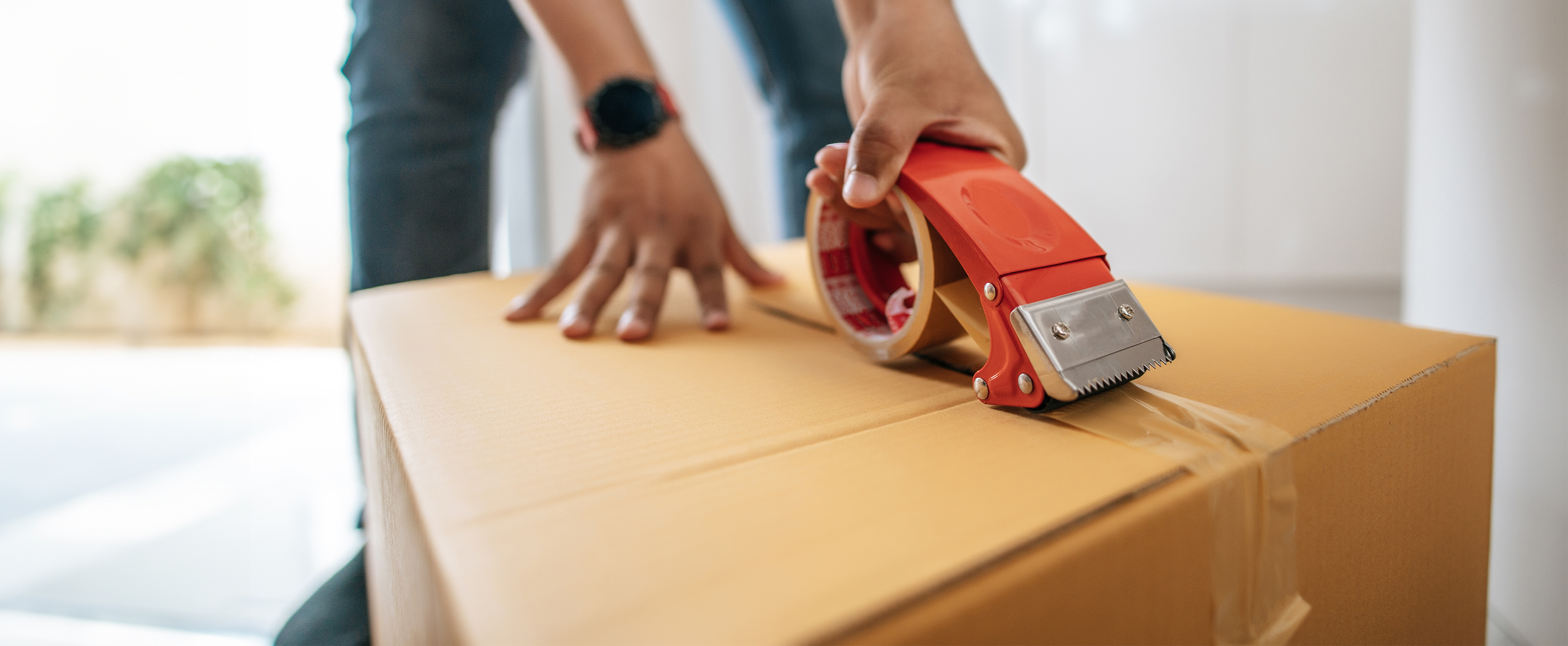 close up photo of someone sealing up a cardboard box using a heavy duty tape dispenser