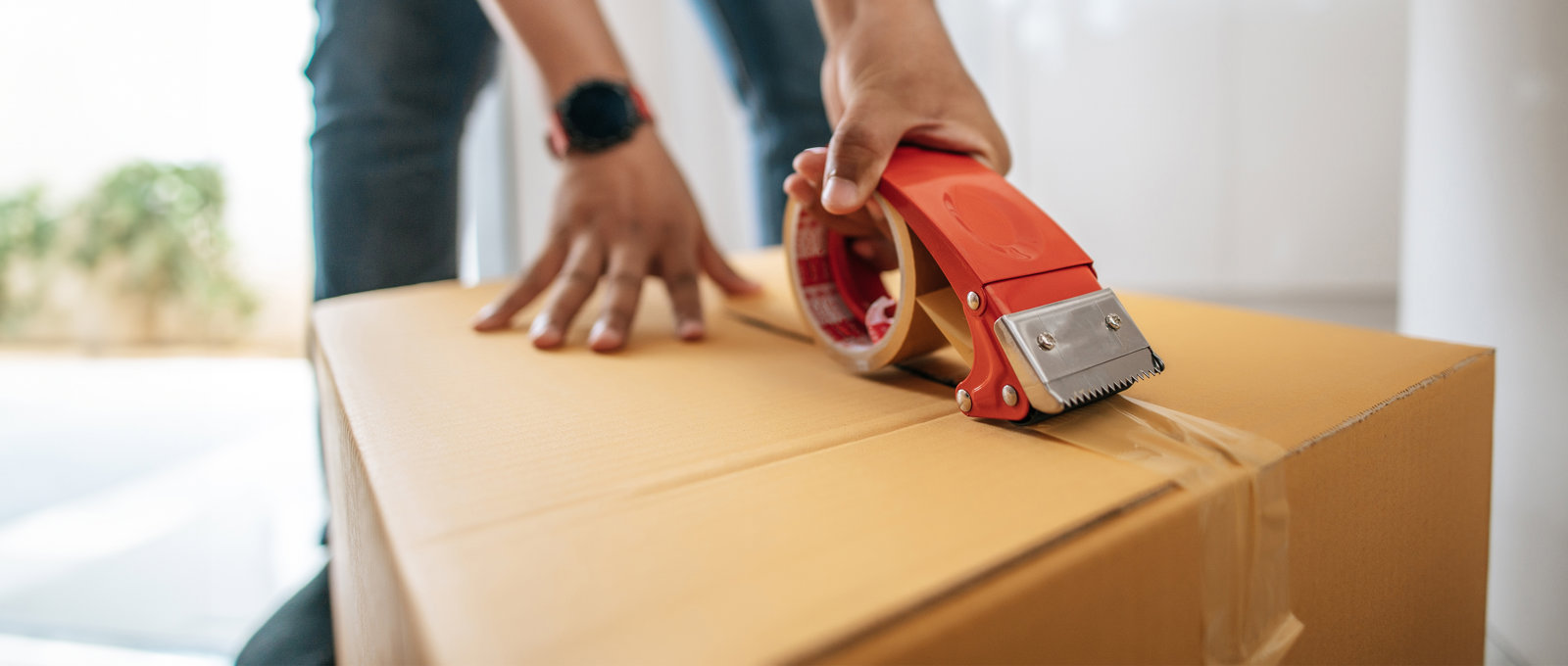 close up photo of someone sealing up a cardboard box using a heavy duty tape dispenser