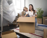 Photo of a young woman and young child smiling at the camera. They are kneeling behind a large cardboard box and surrounded by other boxes