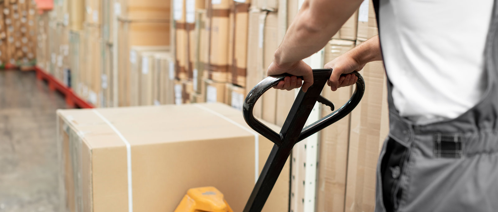 Close up photo of a man pulling a trolley with boxes on it inside a warehouse