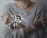 Photo of a woman with her arms closely crossed across her torso. She can be seen reflected in a broken glass mirror