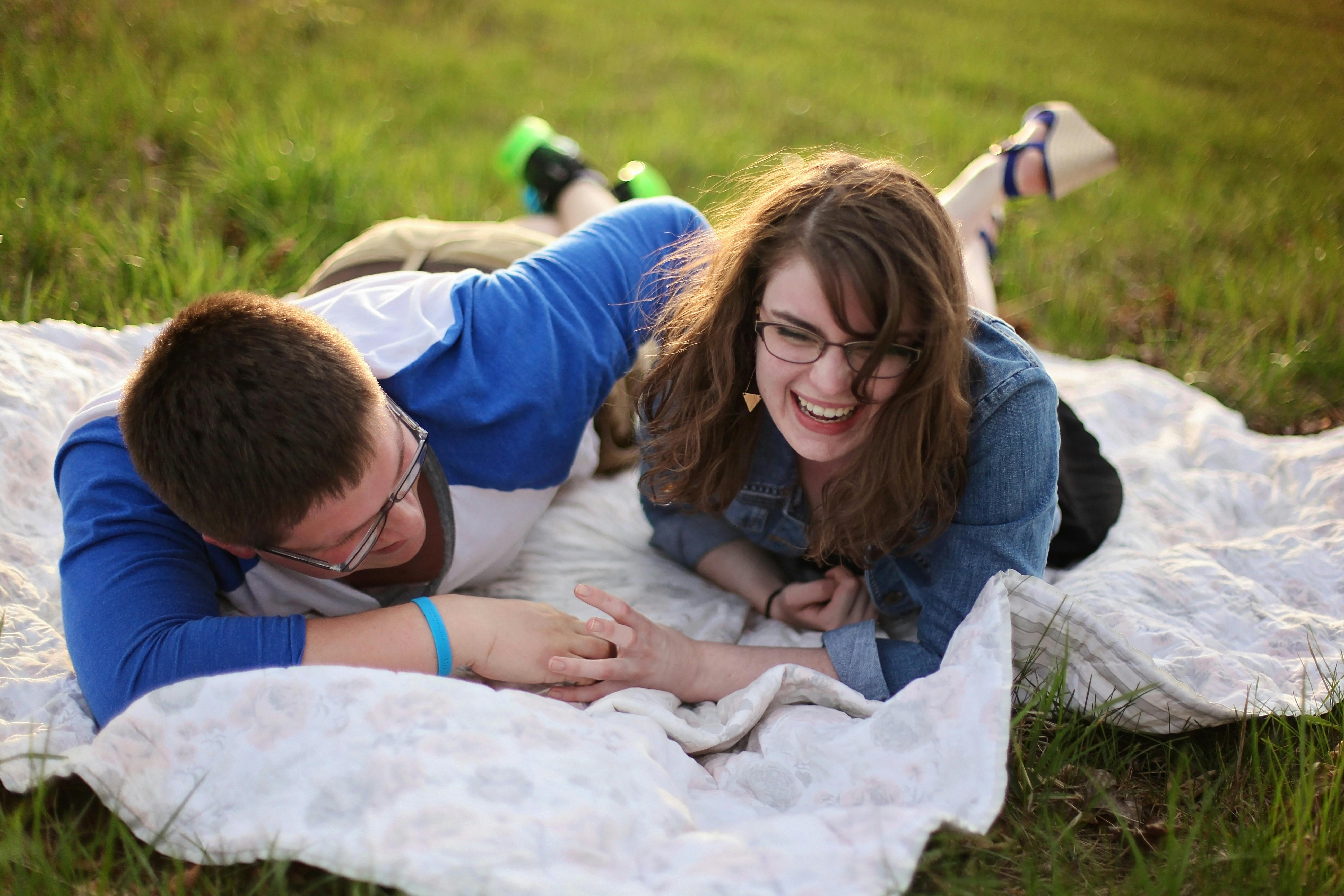A young couple lying on a rug on a grassy area. Both are smiling and laughing.