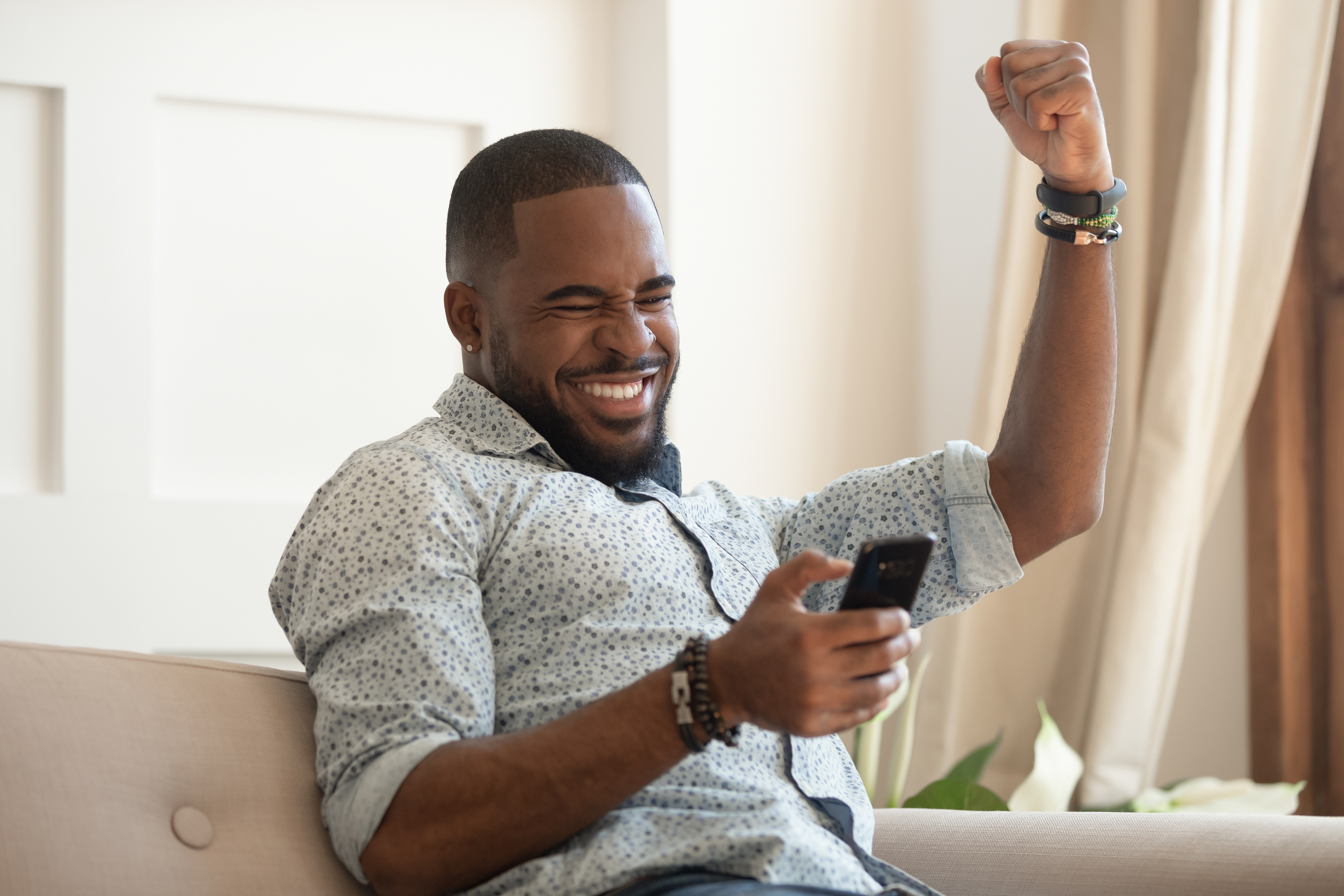 Photograph of a smiling man holding a smart phone and punching the air