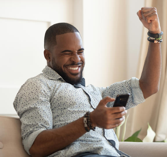 Photograph of a smiling man holding a smart phone and punching the air