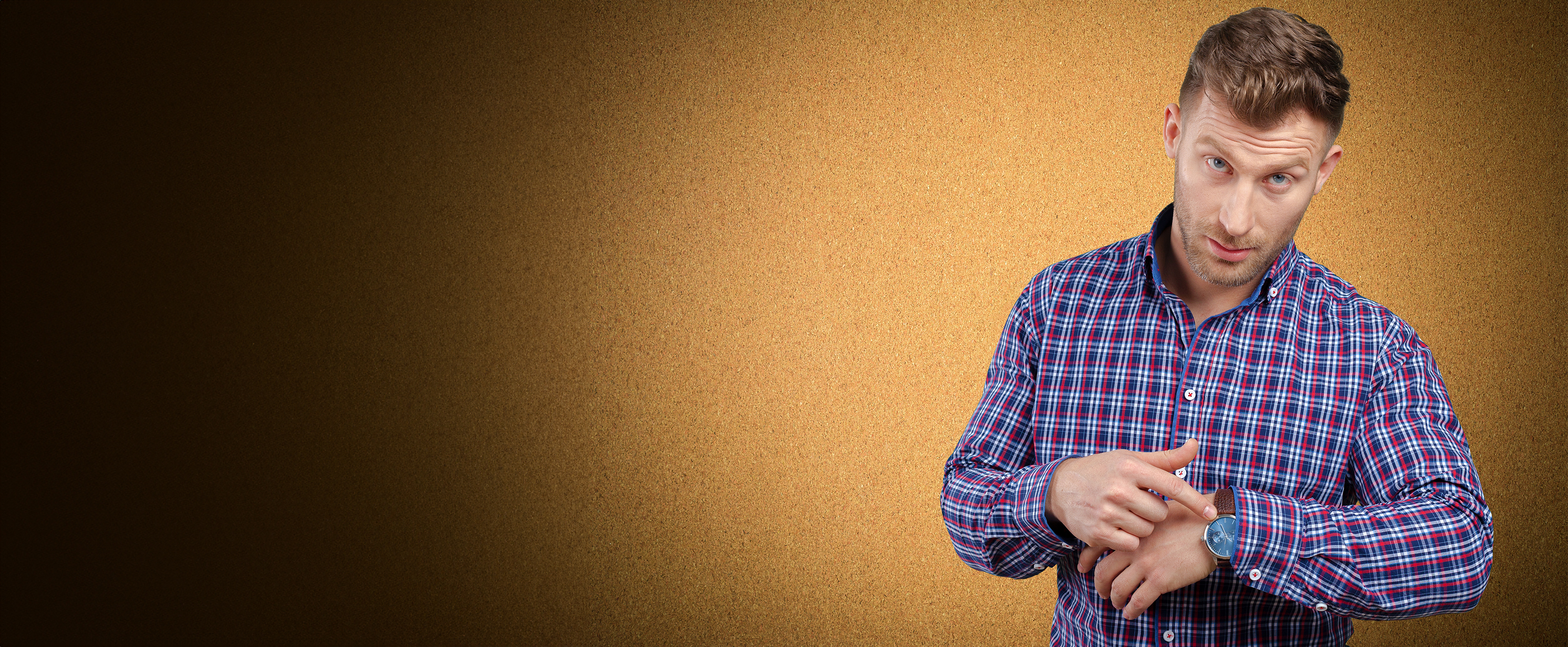 Photo of a man in a checked shirt pointing at his watch and looking towards the camera