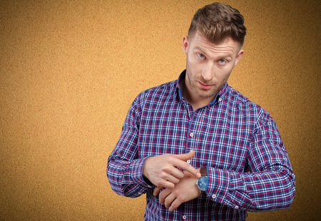Photo of a man in a checked shirt pointing at his watch and looking towards the camera