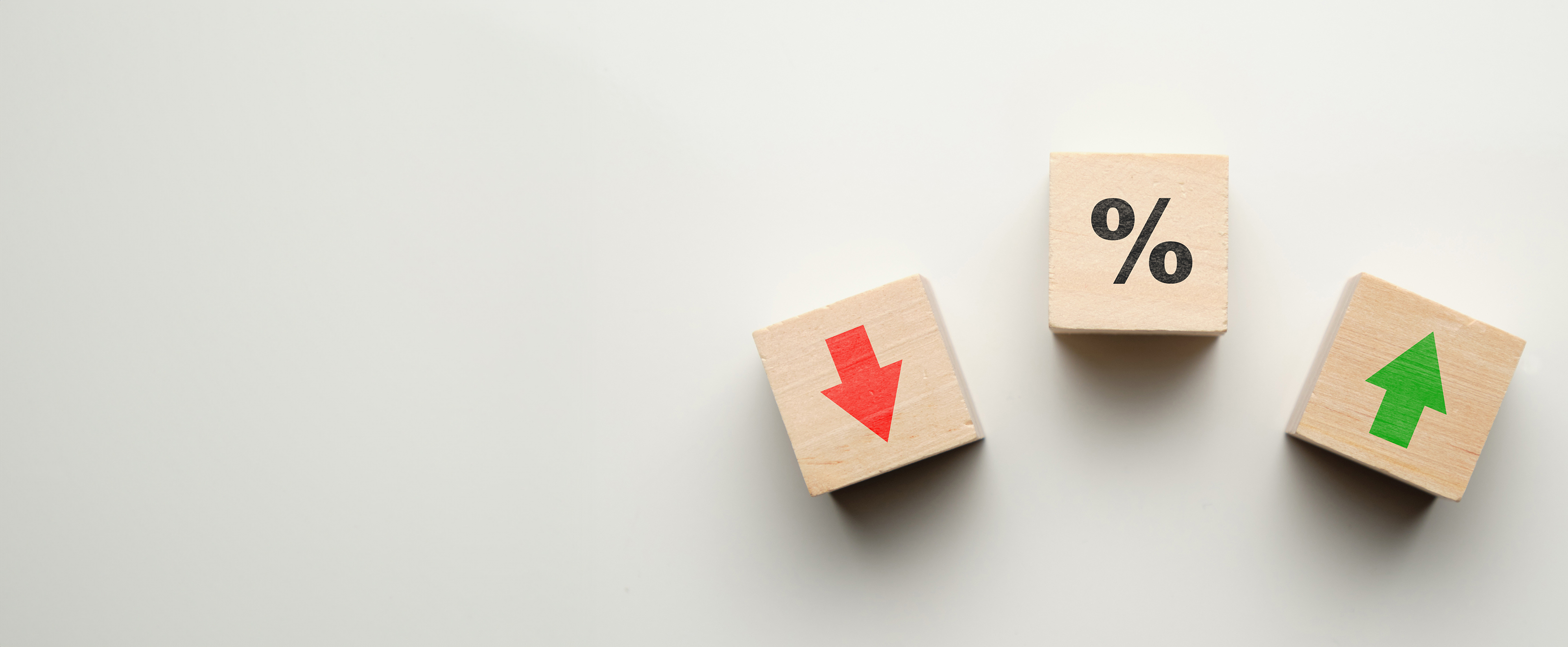 Three wooden blocks on a white surface. The left one has a red-down arrow on it, the centre one has a percentage sign on it, and the right hand one has a green-up arrow on it. 