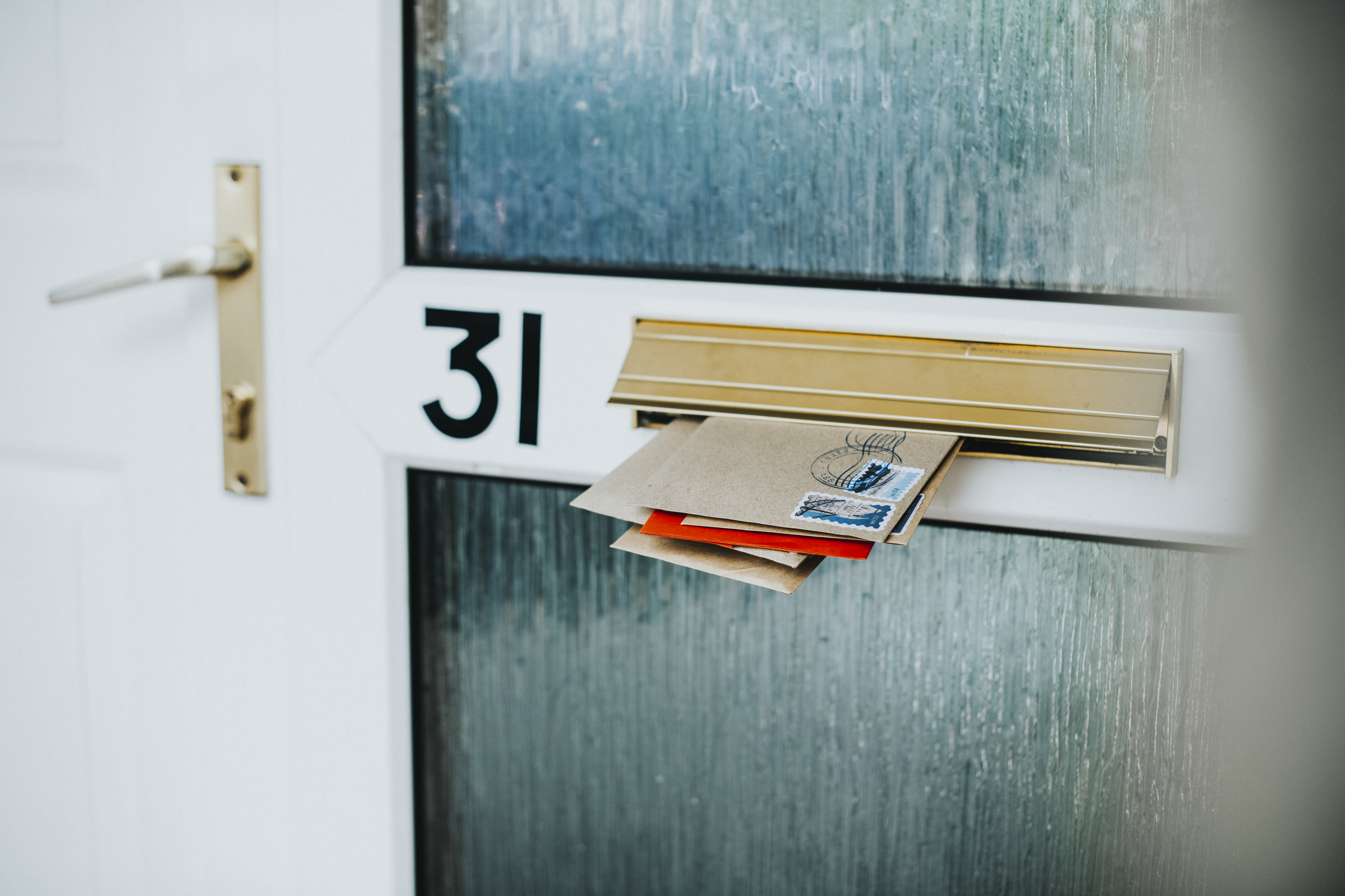 Photo of various envelopes sticking through a letterbox in a house door. The door is numbered with 31.