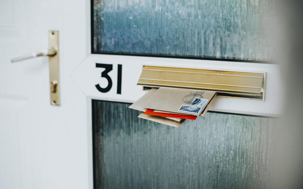 Photo of various envelopes sticking through a letterbox in a house door. The door is numbered with 31.