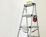 Photo of a stepladder in a white painted room. The ladder has various items of protective wear hanging on it.