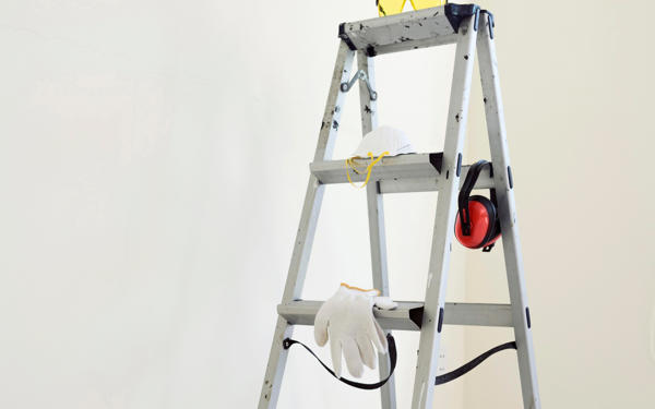 Photo of a stepladder in a white painted room. The ladder has various items of protective wear hanging on it.