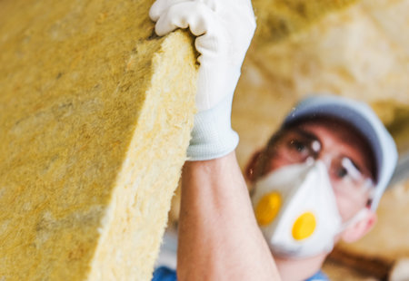 Photo of a man in a roof space wearing a protective mask holding a large sheet of insulation material towards the camera