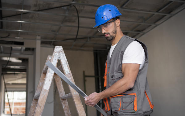 Photo of a workman standing in a property under construction. He is wearing a hard hat and other protective clothing