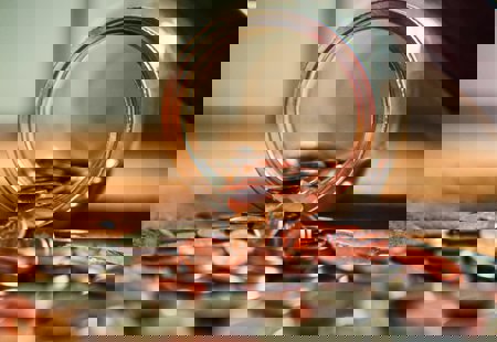 close up photo of a glass jar lying overturned on a surface with lots of coins spilling out of it onto the surface
