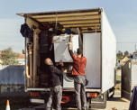 Photo of two man putting a fridge into the back of a truck filled with other household items