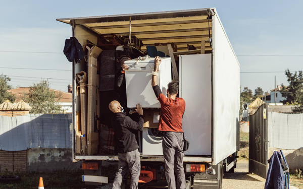 Photo of two man putting a fridge into the back of a truck filled with other household items