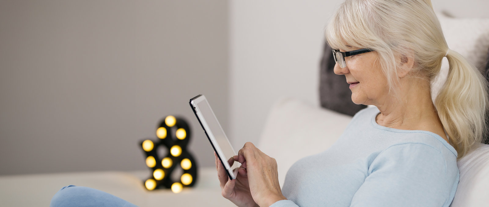 Photo of an older woman wearing glasses sitting on a sofa and using a tablet computer