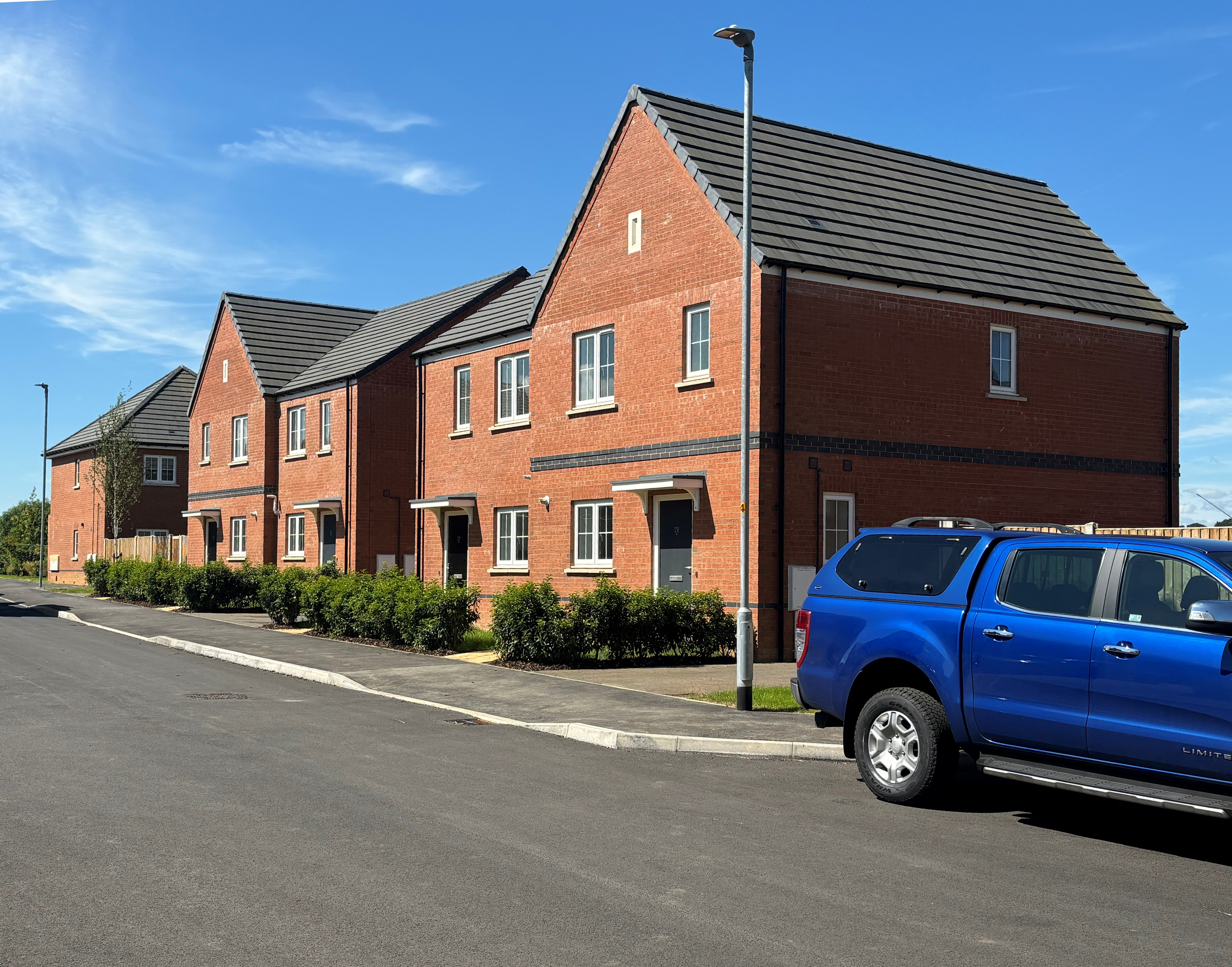 Photo of a small terrace of new build houses with a blue pickup truck in the foreground