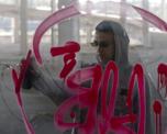 Photo of a man in sunglasses and a hoodie spraying red graffiti on glass - viewed from the other side of the glass