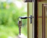 Close up photo of a key inserted in a door lock. We can see a garden in the background where the door is open