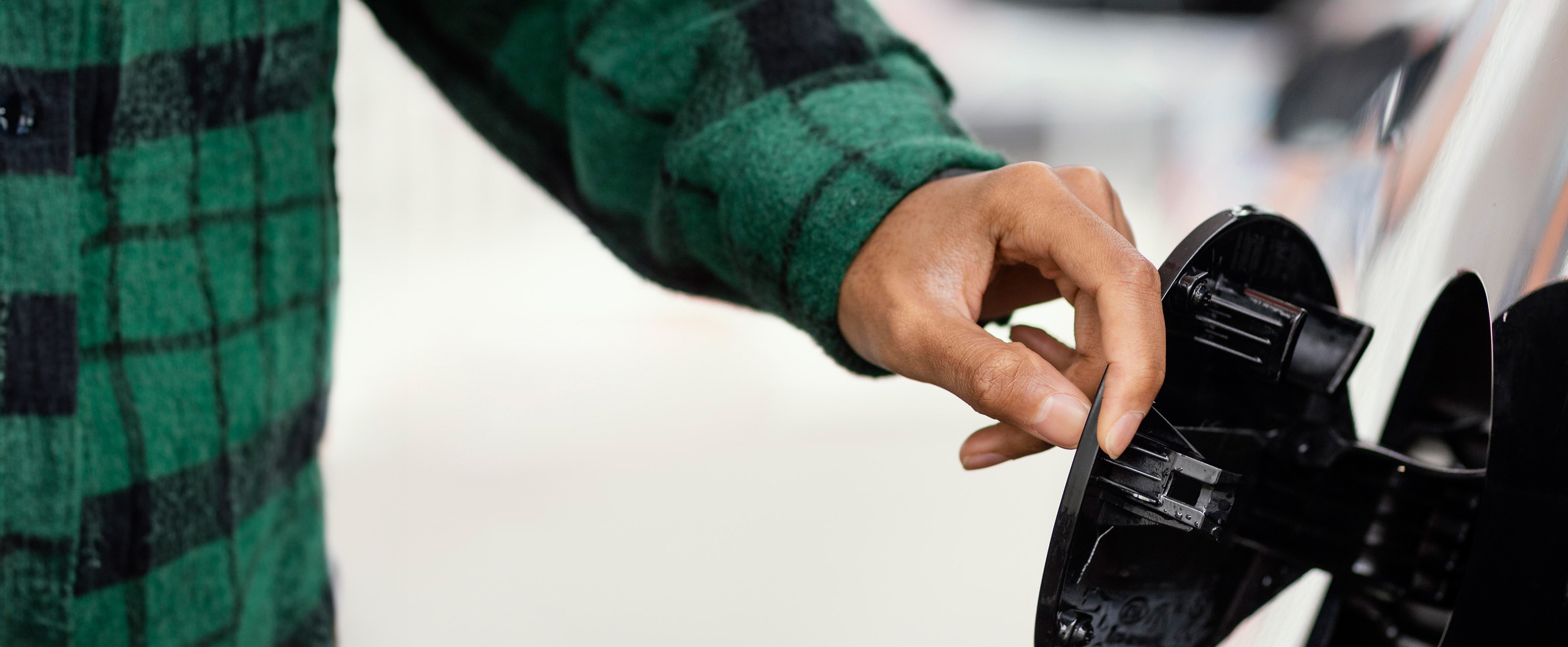 close up photo of a man's hand opening the petrol filler flap on a vehicle
