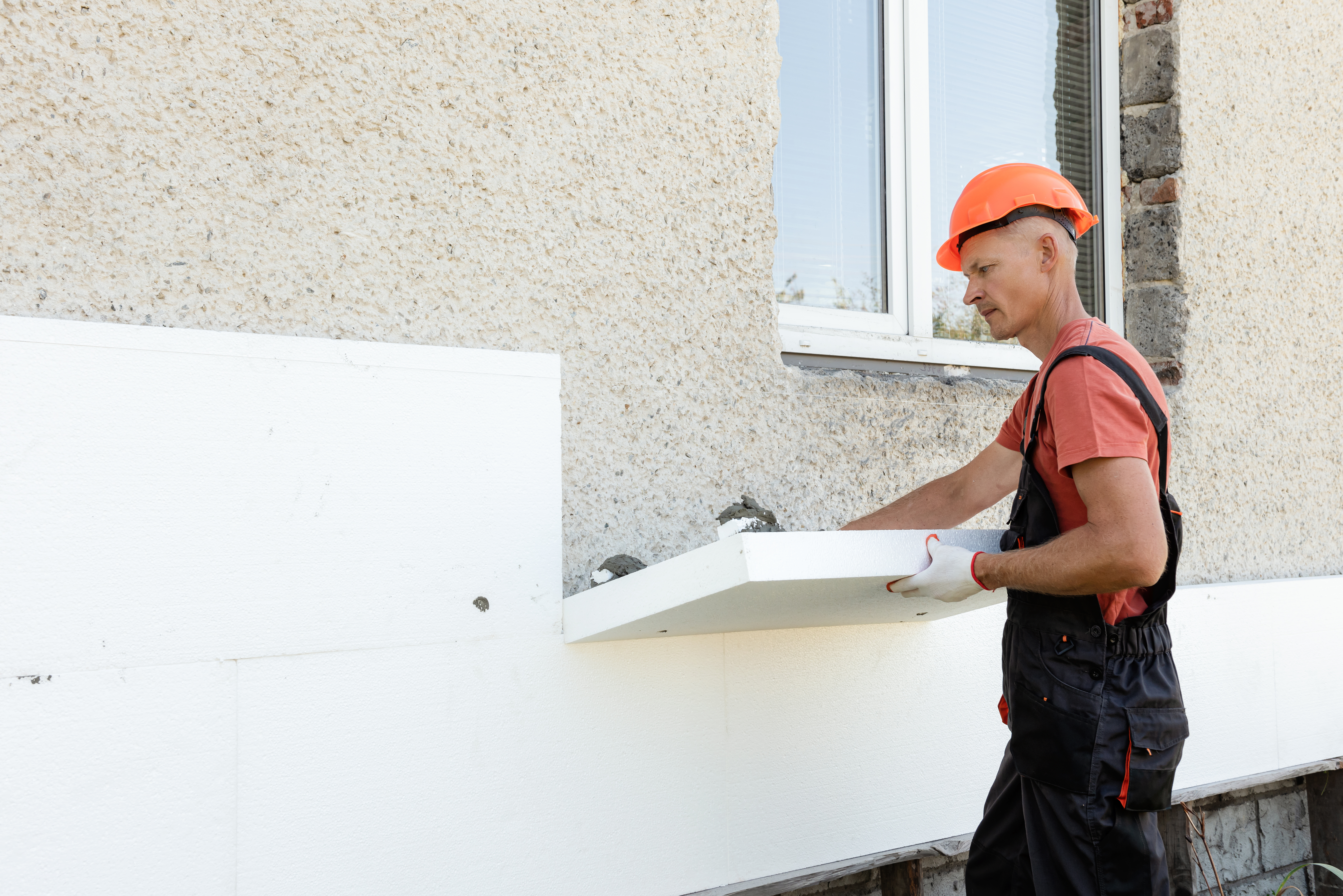 Photo of a workman in a hard hat installing insulation boards on an external wall
