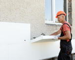 Photo of a workman in a hard hat installing insulation boards on an external wall