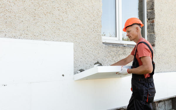 Photo of a workman in a hard hat installing insulation boards on an external wall