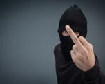 Photo of a man with his face partially covered by black facemask and he is raising a finger towards the camera in a threatening way