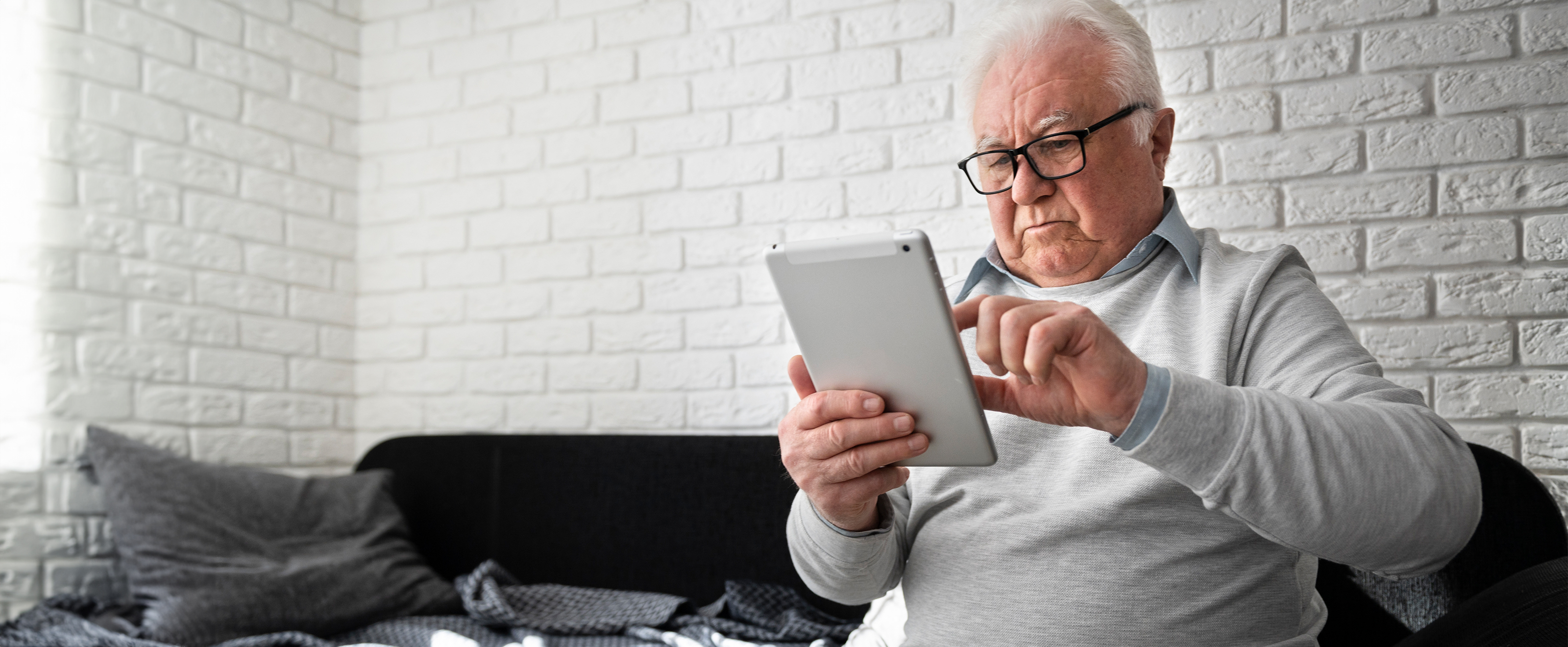 Photo of an older man using a tablet computer while sitting on a sofa