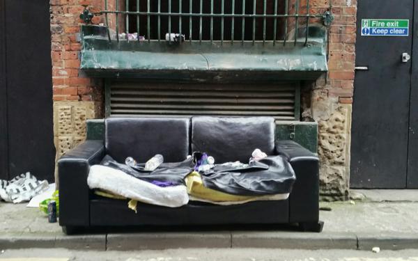 Photo of a ruined black leather sofa dumped in a city street