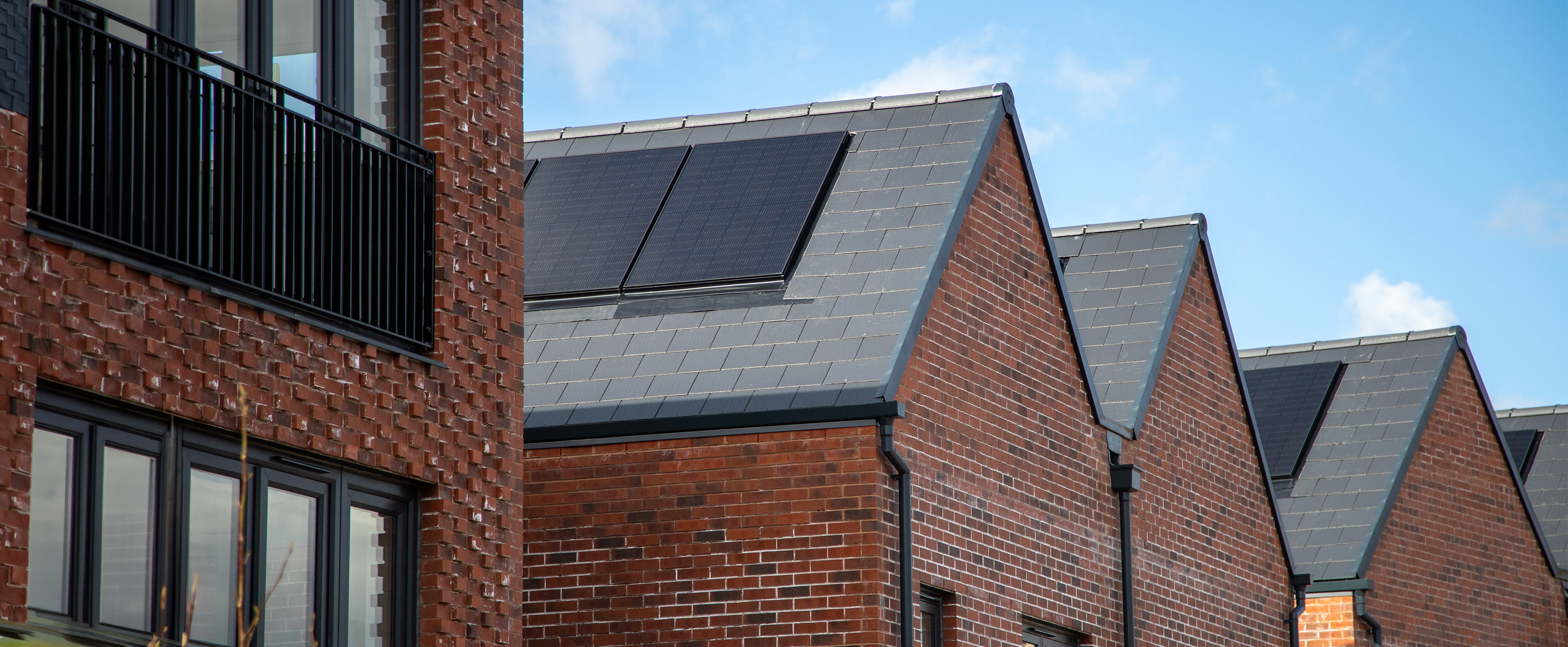 Photograph looking across the sloping roofs of several modern houses. Solar panels have been installed.