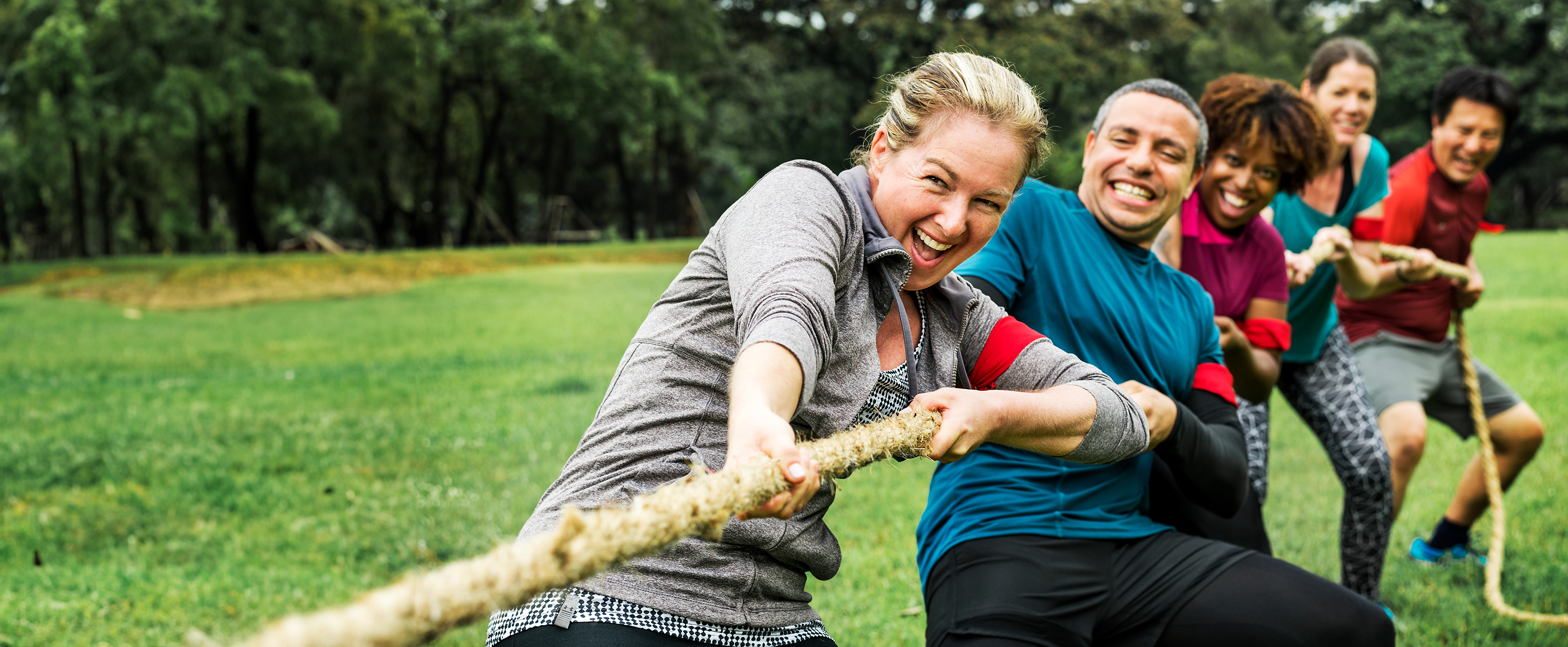 Photo of five people of various ages taking part in a tug of war - they are pulling the rope away from the viewer